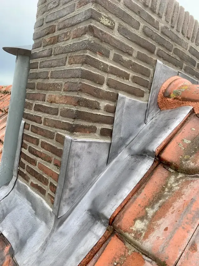 Schoorsteen boven rode pannen — Metselwerk en loodwerk bij een schoorsteen op een rood pannendak.